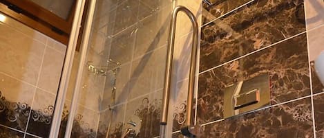 A modern bathroom with a glass shower enclosure, a marble-tiled wall, and a white toilet.