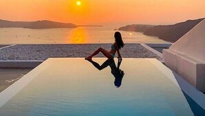 Una persona sentada en una piscina infinita con vistas al atardecer.