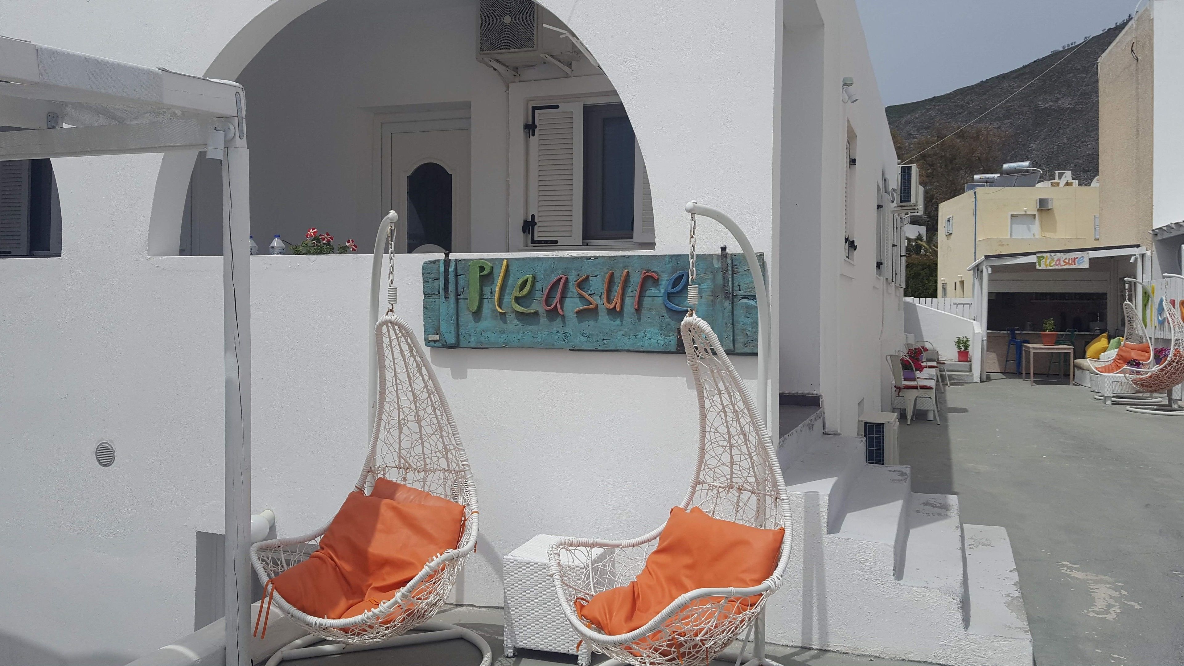 A white building with a sign reading "Pleasure" and two white wicker chairs with orange cushions.