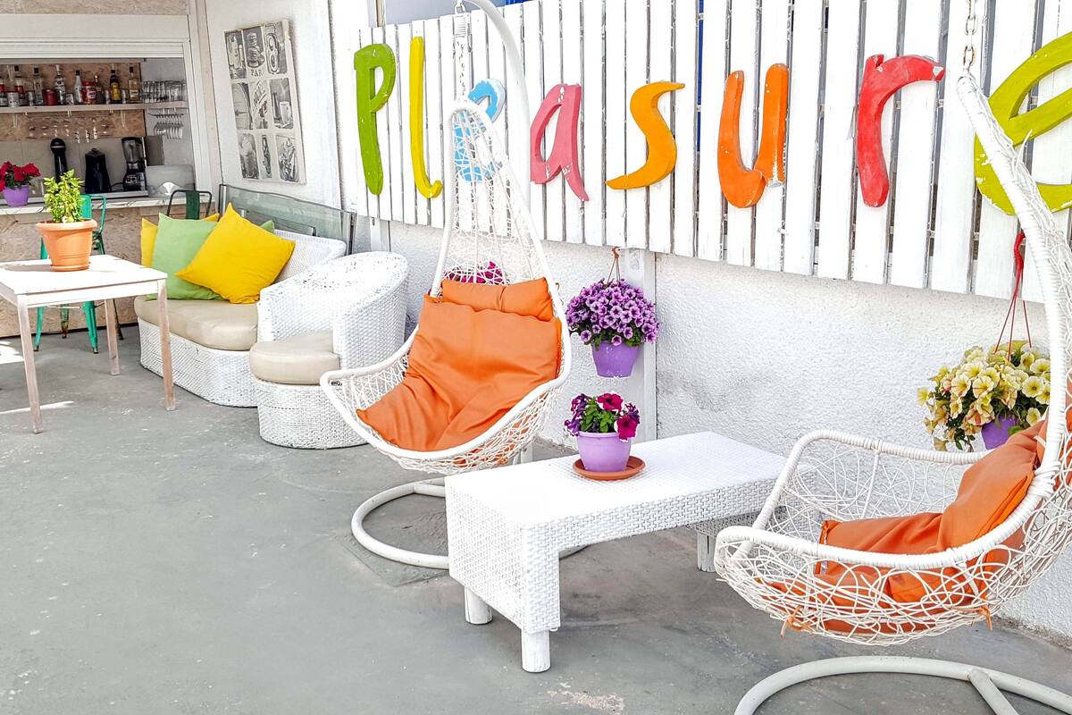 A patio area with wicker furniture, including chairs and a table, and a wall with the word 'Plaisure' spelled out in colorful letters.
