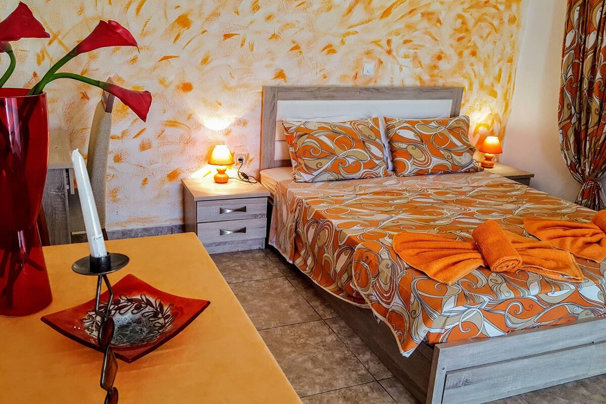 A bedroom with a bed, bedside tables, a nightstand, a vase with flowers, and a lamp.