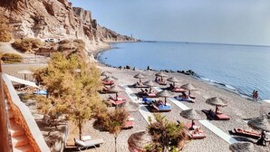 Una playa con tumbonas y sombrillas, un acantilado rocoso y una vista despejada del mar.