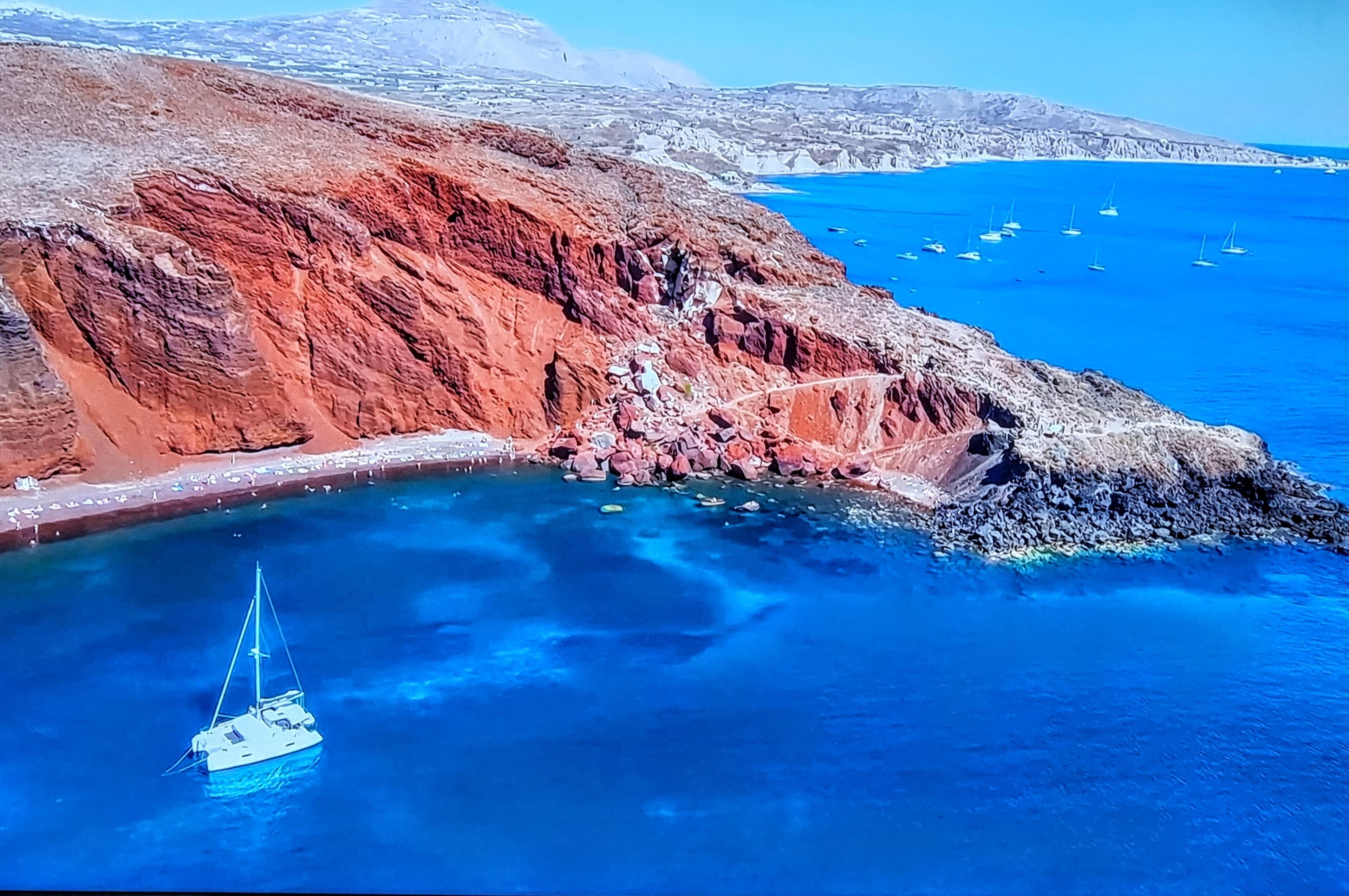 A coastal landscape with a rocky cliff, clear blue sea, and a sailboat.