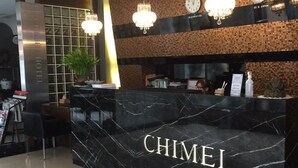 A hotel reception desk with a black marble front, a chandelier, and a clock on the wall. - CHIMEI Hotel (Taoyuan City)