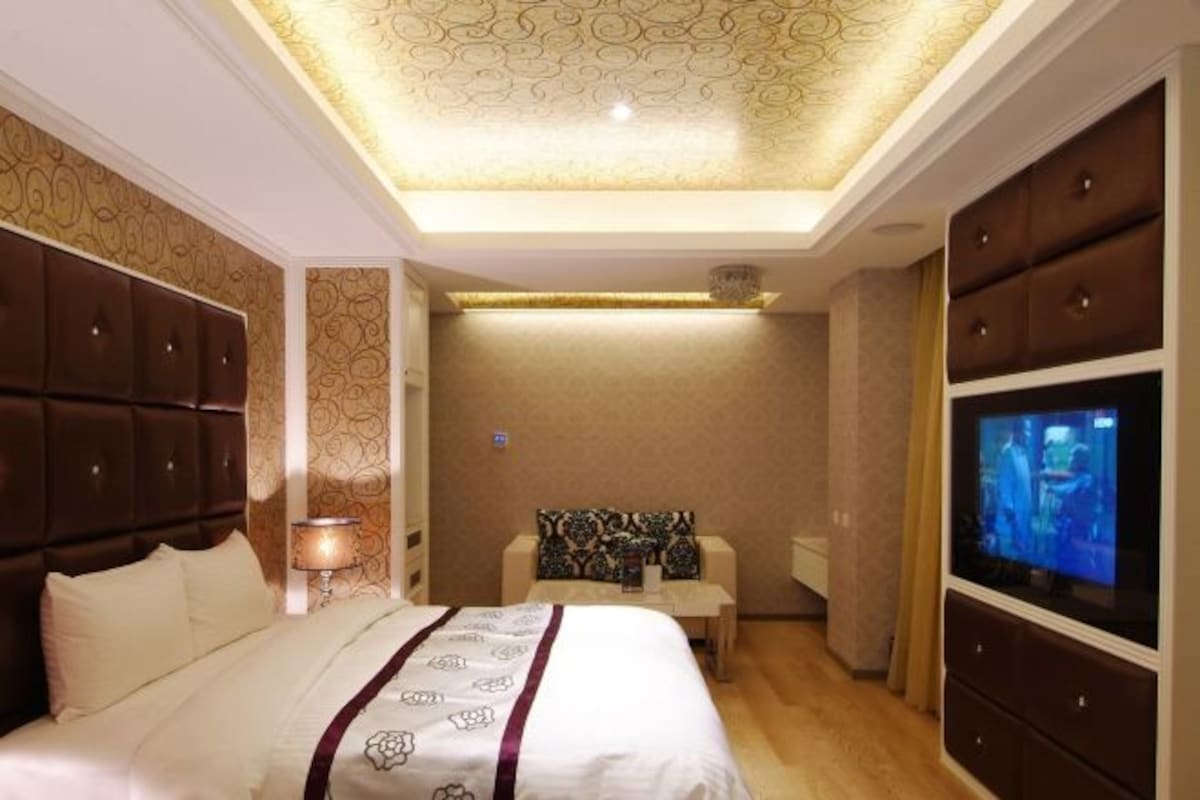 A hotel room with a large bed, a TV, a desk, and a sofa.