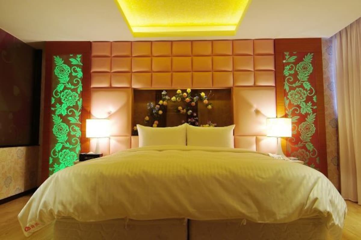 A hotel room with a large bed, a padded headboard, and decorative wall panels.