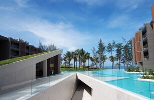 A modern hotel with a swimming pool, palm trees, and a clear blue sky.