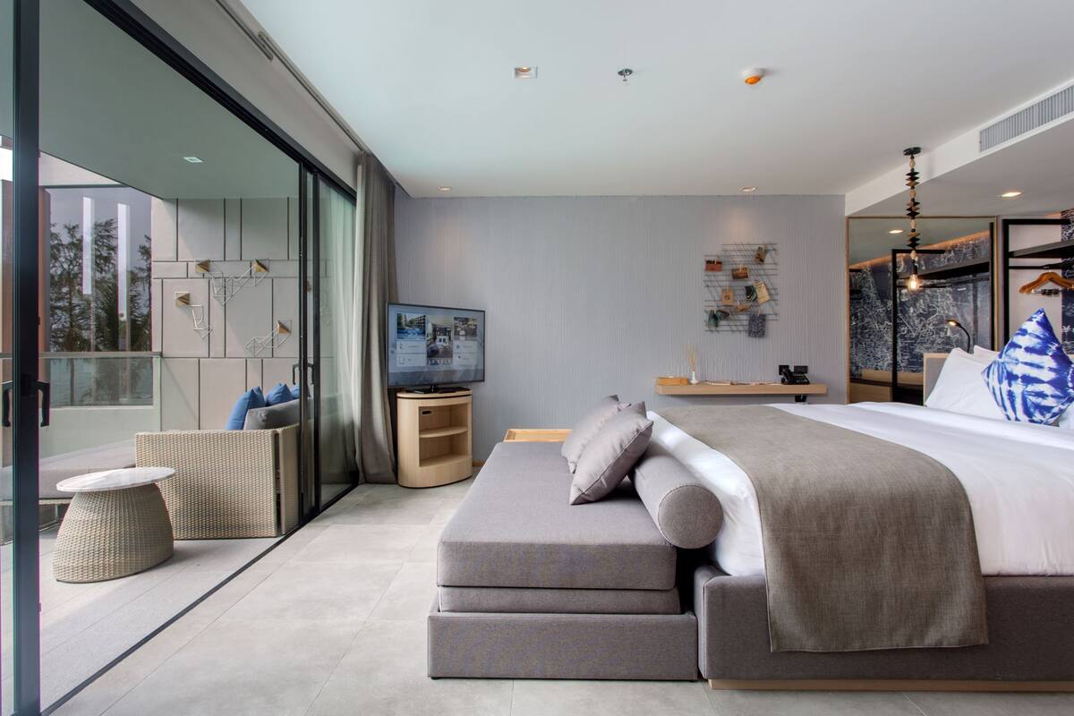 Een moderne slaapkamer met een groot bed, een televisie en een balkon met rieten meubels.