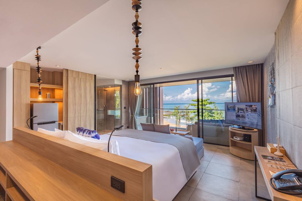 Une chambre d’hôtel moderne dotée d’un grand lit, d’un bureau en bois, d’une télévision et d’un balcon offrant une vue sur l’océan.