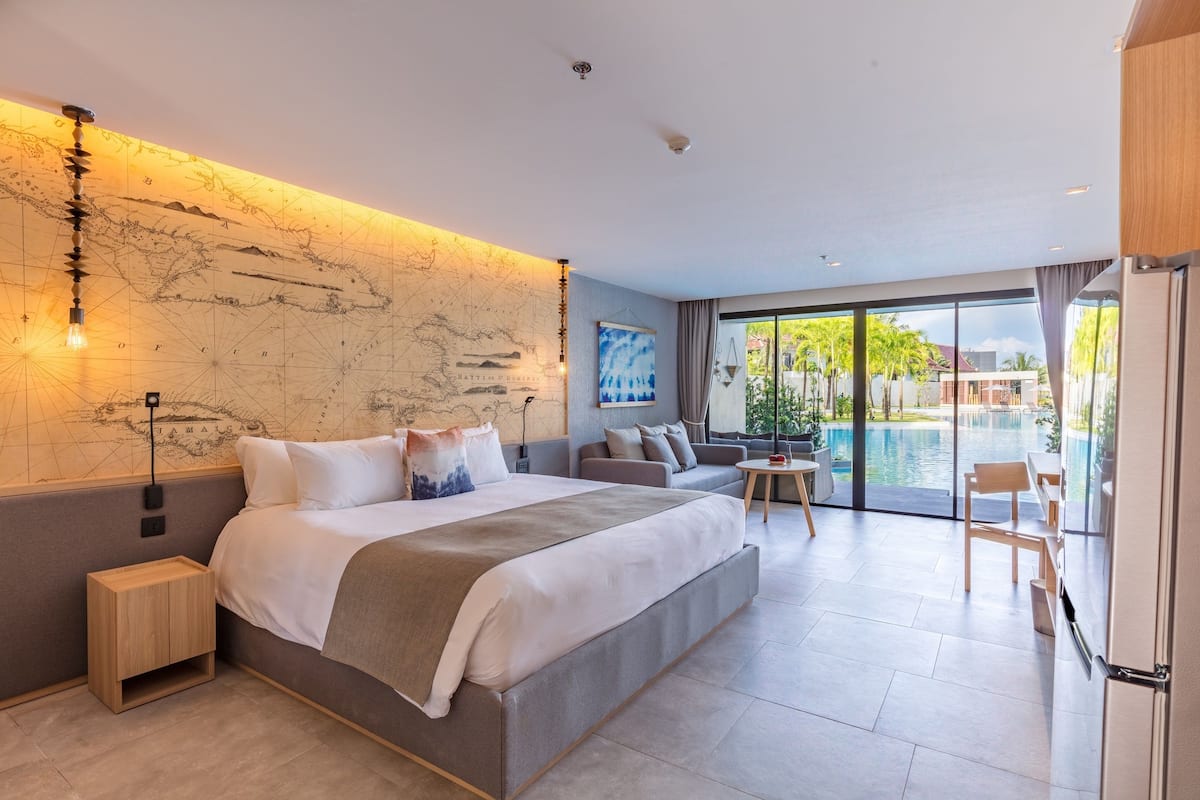 Une chambre moderne avec un grand lit, un mur décoré d’une carte, un canapé et une vue sur une piscine extérieure.