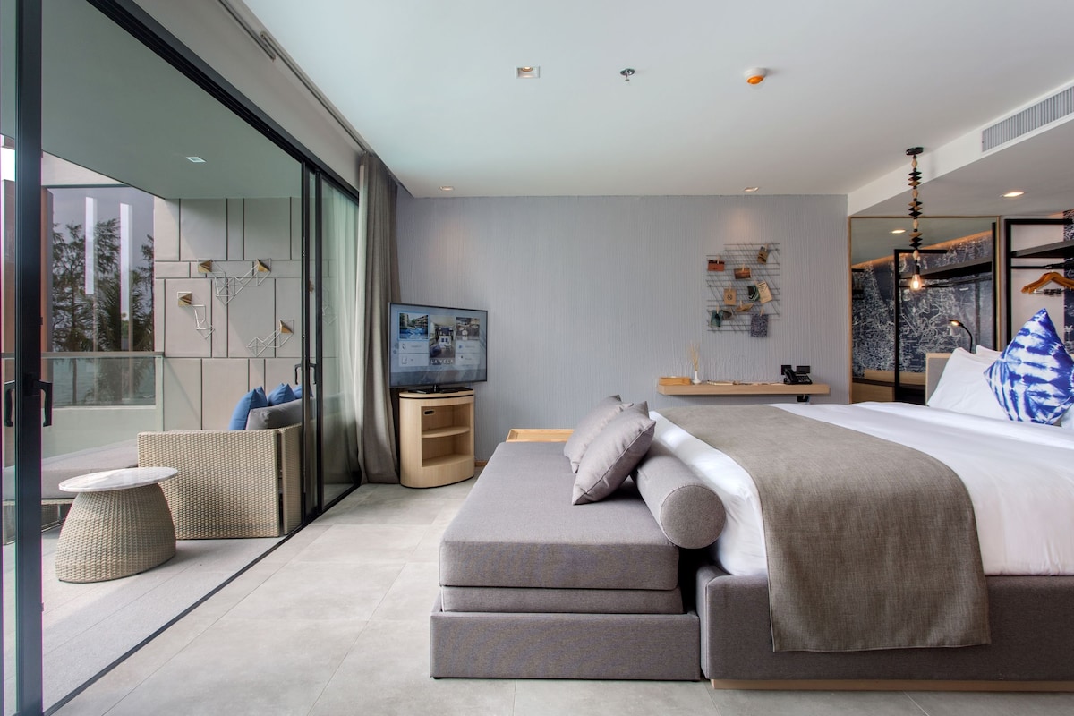 Een moderne slaapkamer met een groot bed, een televisie en een balkon met rieten meubels.