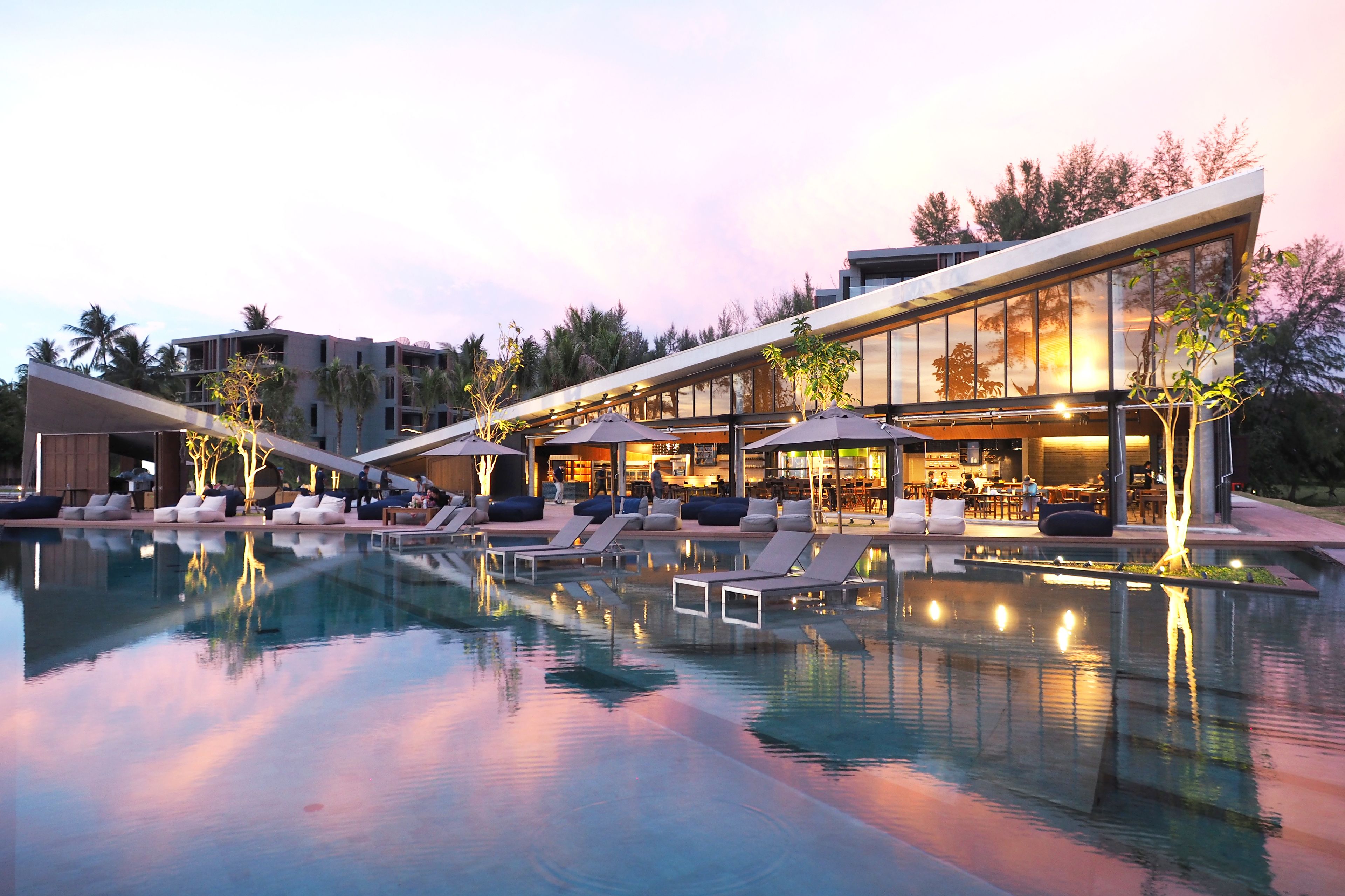 Un hotel moderno con piscina, sillas de descanso y zona de restaurante.