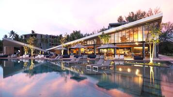 Un hotel moderno con piscina, sillas de descanso y zona de restaurante.