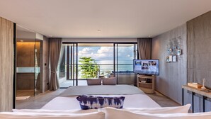 A modern hotel room with a large bed, a TV, and a balcony with a view of the ocean.
