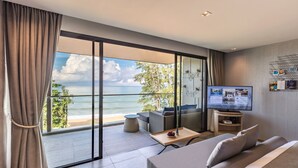 A modern hotel room with a large balcony overlooking the beach, a flat-screen TV, and a comfortable seating area.