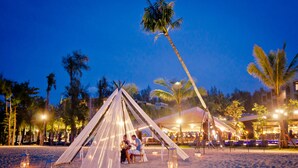 A beach setting with a tent structure, palm trees, and a sandy beach.