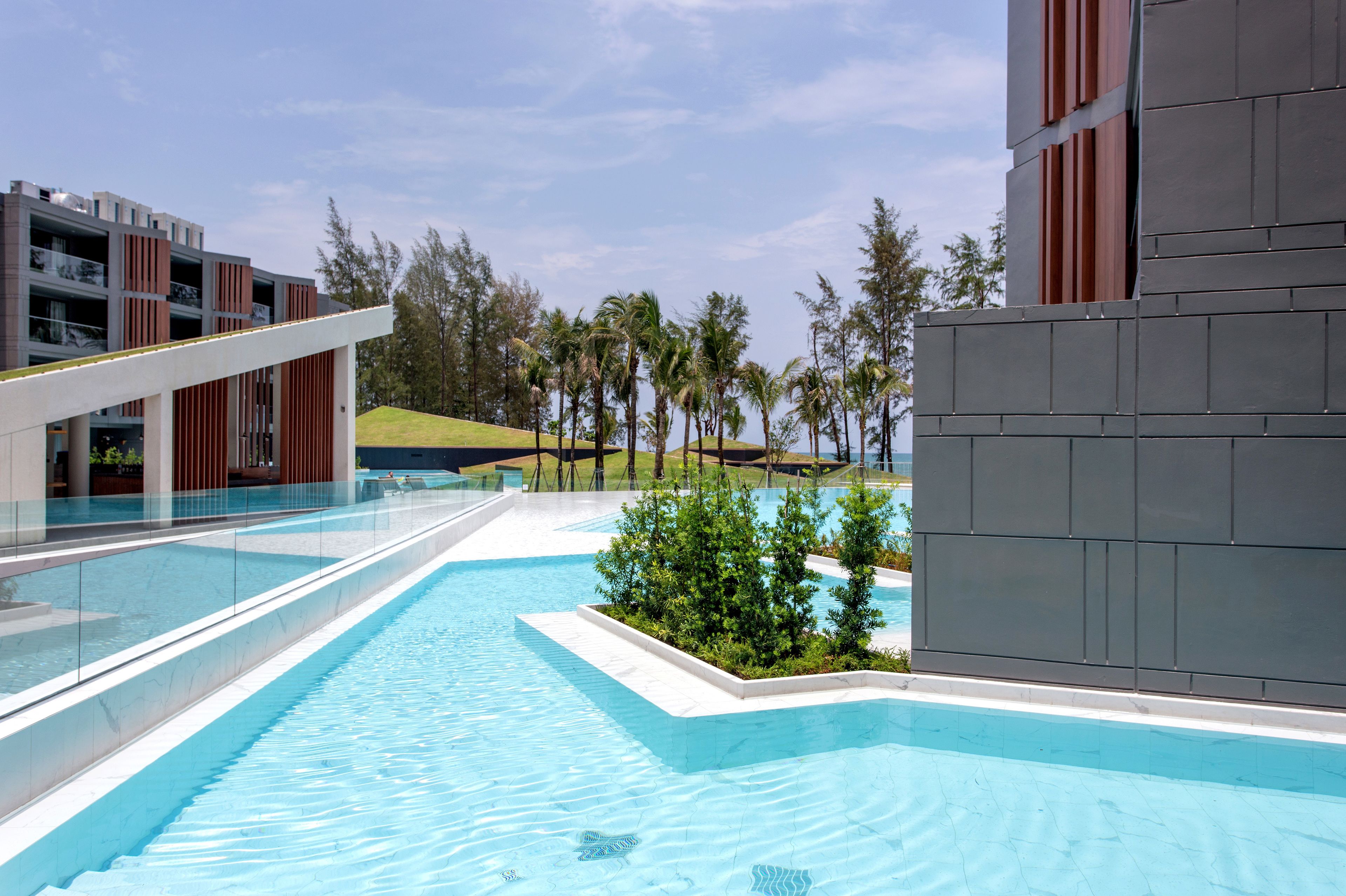 A modern pool area with clear blue water, surrounded by a glass railing, and adjacent to a building with a red facade and a flat roof.