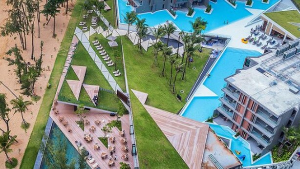 An aerial view of a resort with multiple swimming pools, a central courtyard, and surrounding buildings.