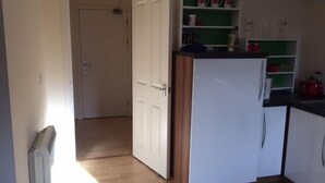 A kitchen with white cabinets, a refrigerator, and a green shelf with kitchenware. - 6 Varis Apartments (Forres)