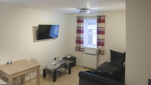 A living room with a flat-screen TV mounted on the wall, a sofa, a coffee table, and a dining table with chairs. - 6 Varis Apartments (Forres)