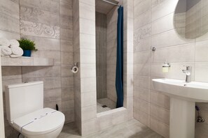 Een badkamer met toilet, douche met gordijn, wastafel en spiegel.