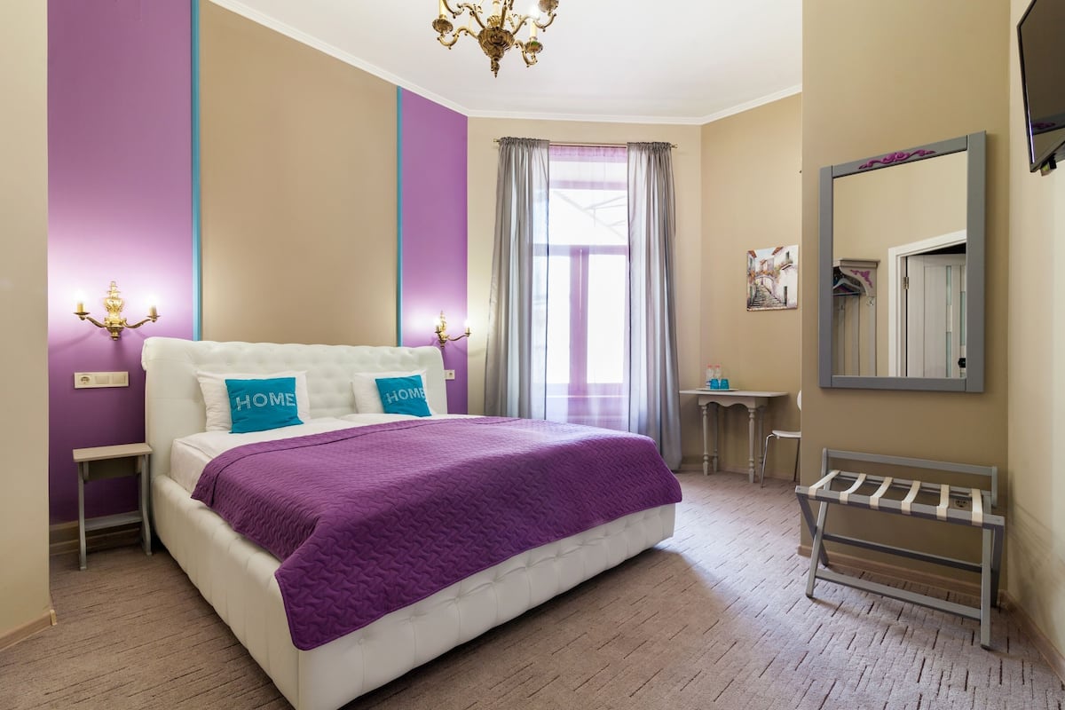 Un dormitorio con cama, mesita de noche, escritorio, silla, espejo y ventana con cortinas.