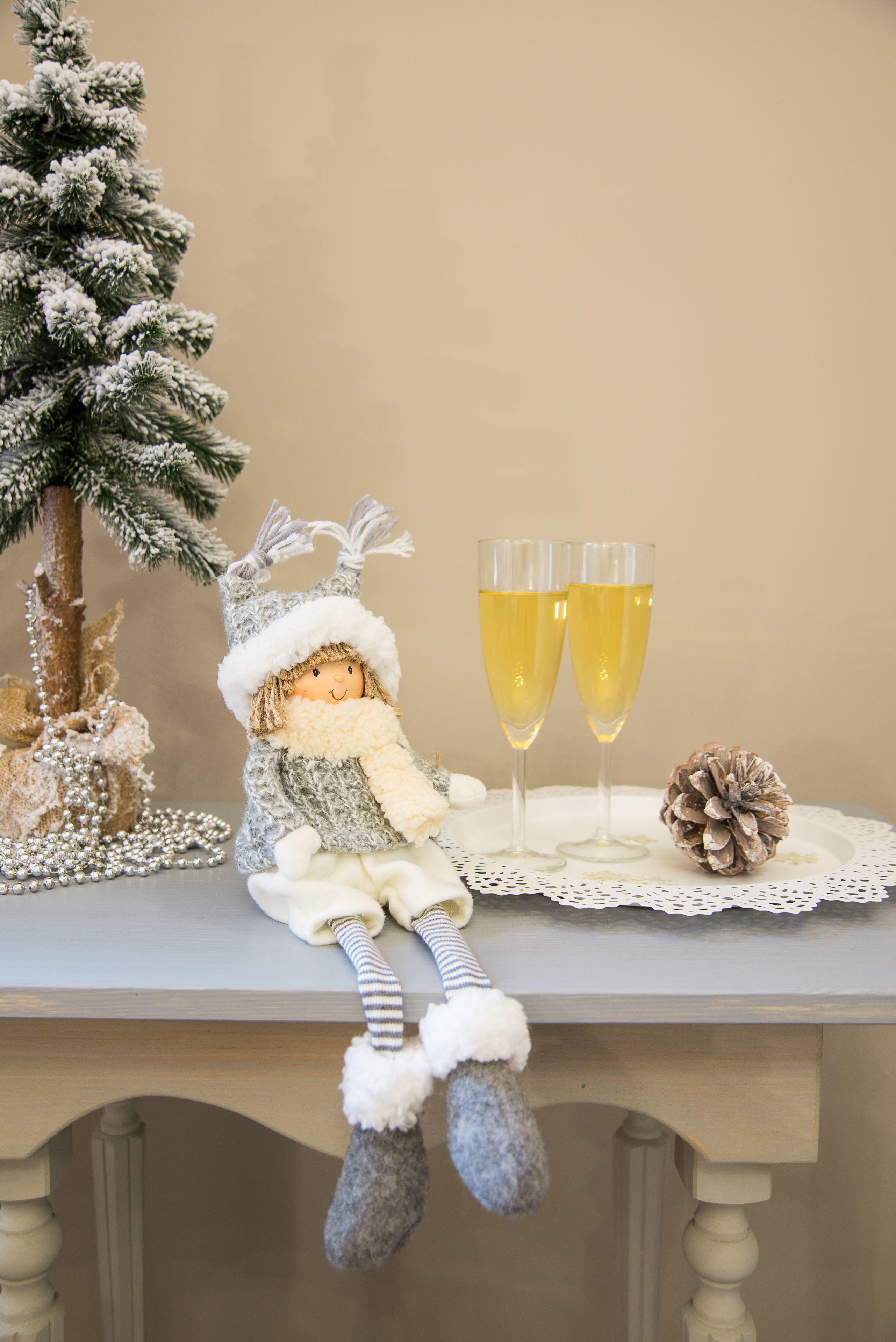 A doll with a hat and boots sitting on a table with two glasses of champagne and a pine cone.