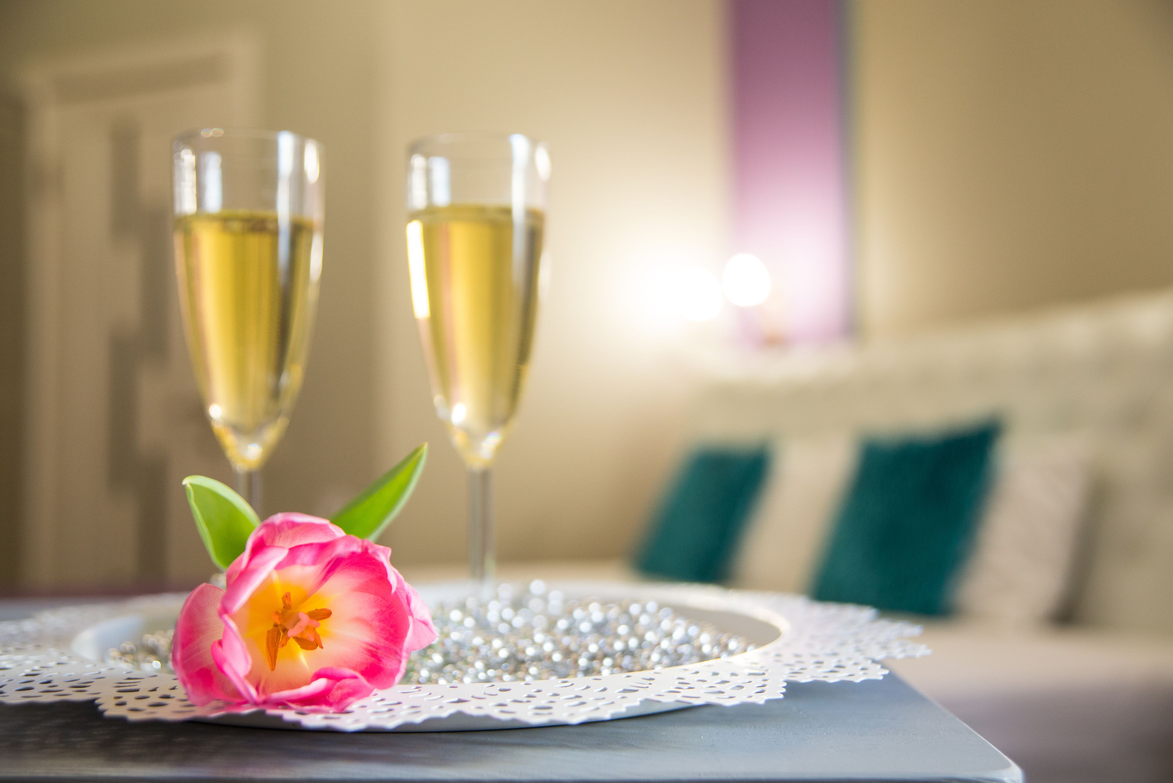 Uma mesa com duas taças de champanhe e uma tulipa rosa sobre um sousplat rendado.