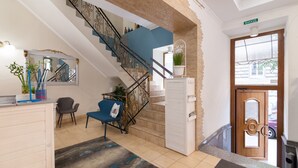 Een hotel lobby met een trap, een receptiebalie, een blauwe stoel en een houten deur.