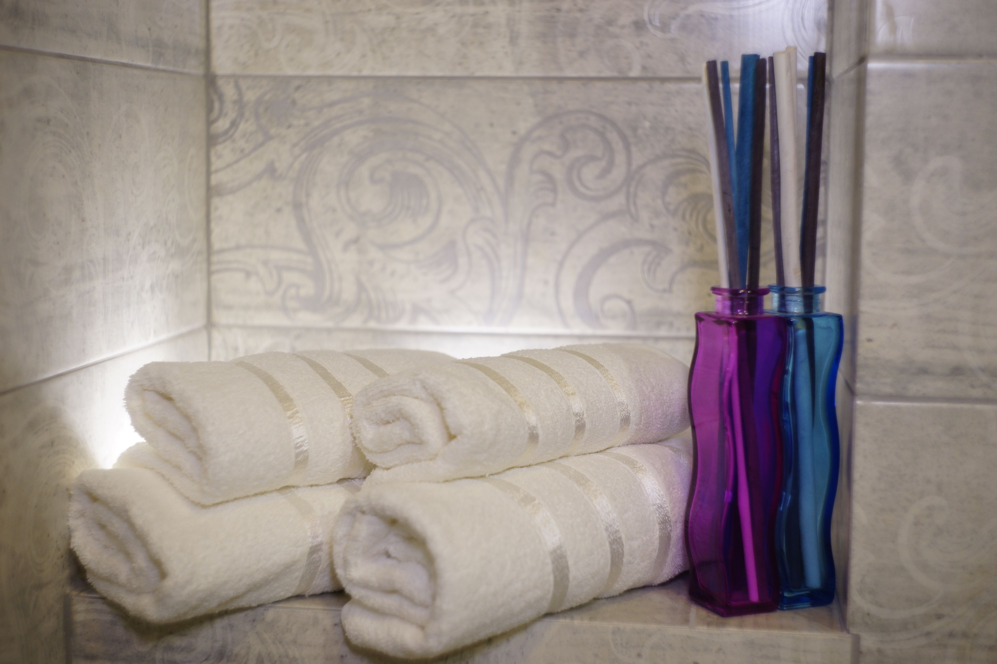 A bathroom with a marble wall, a towel rack with folded towels, and a glass vase with pens.