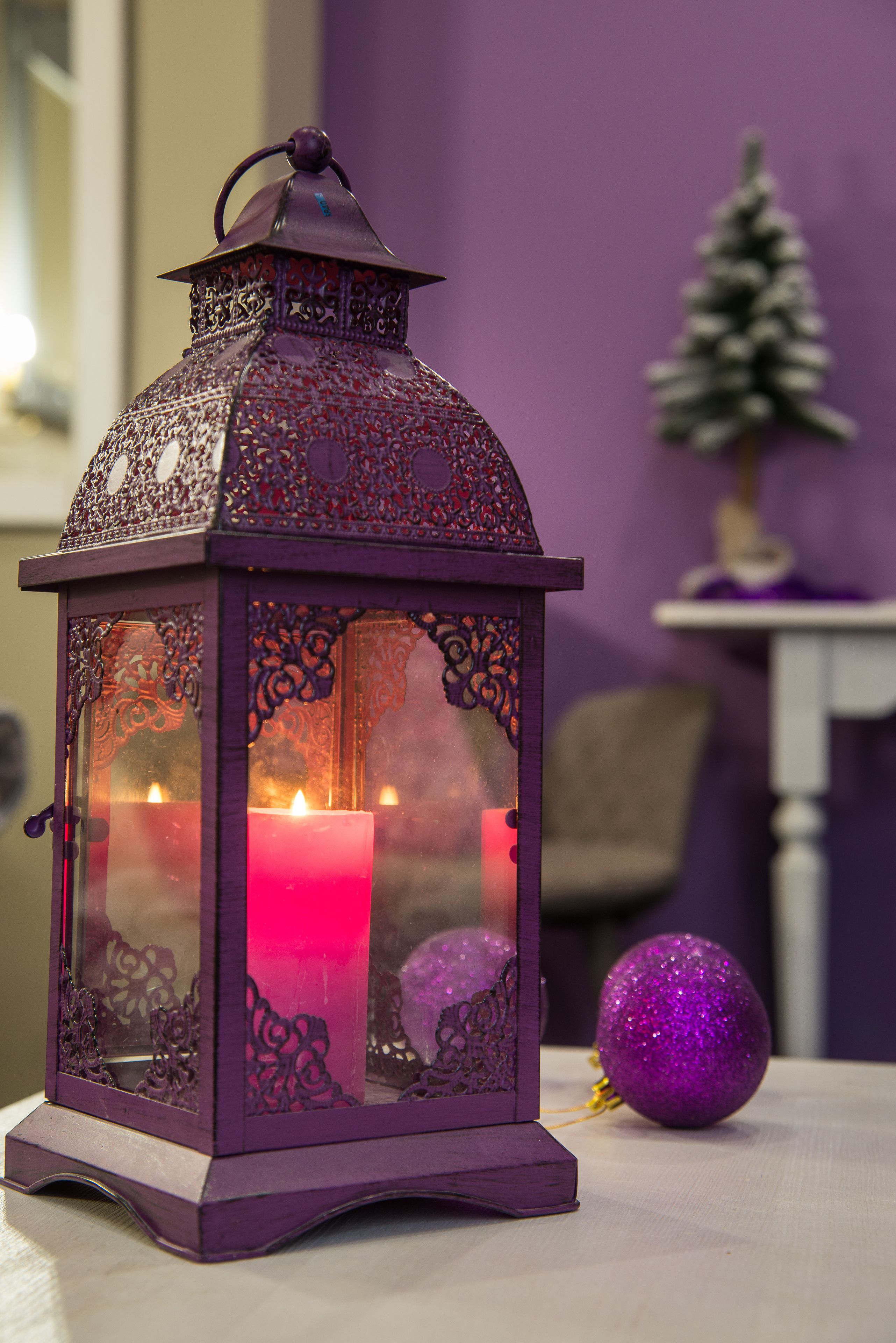 Une lanterne violette aux motifs complexes, avec une bougie allumée à l’intérieur, posée sur une table.