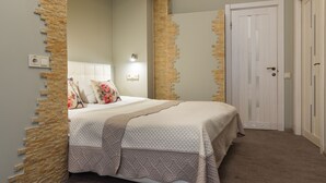 Een slaapkamer met een bed, een accentmuur van steen, een witte deur en een nachtkastje met een lamp.