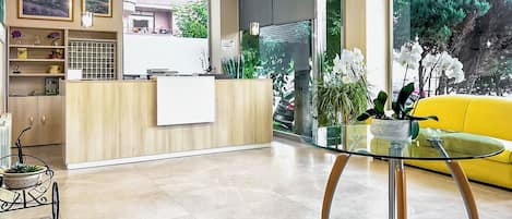 A modern reception area with a wooden reception desk, a glass table, and a yellow sofa.