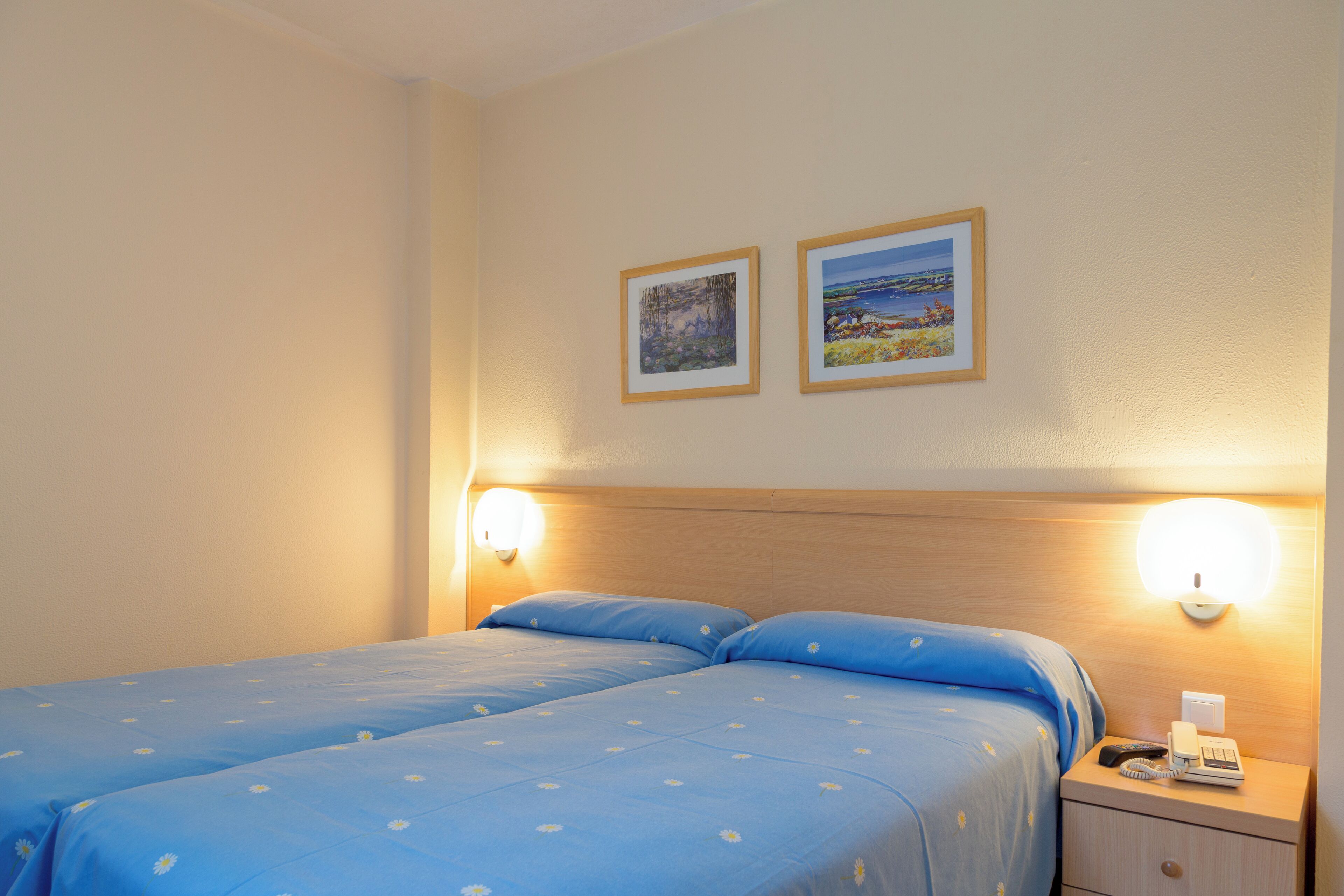 A double bed with blue bedding and two wall-mounted lamps.
