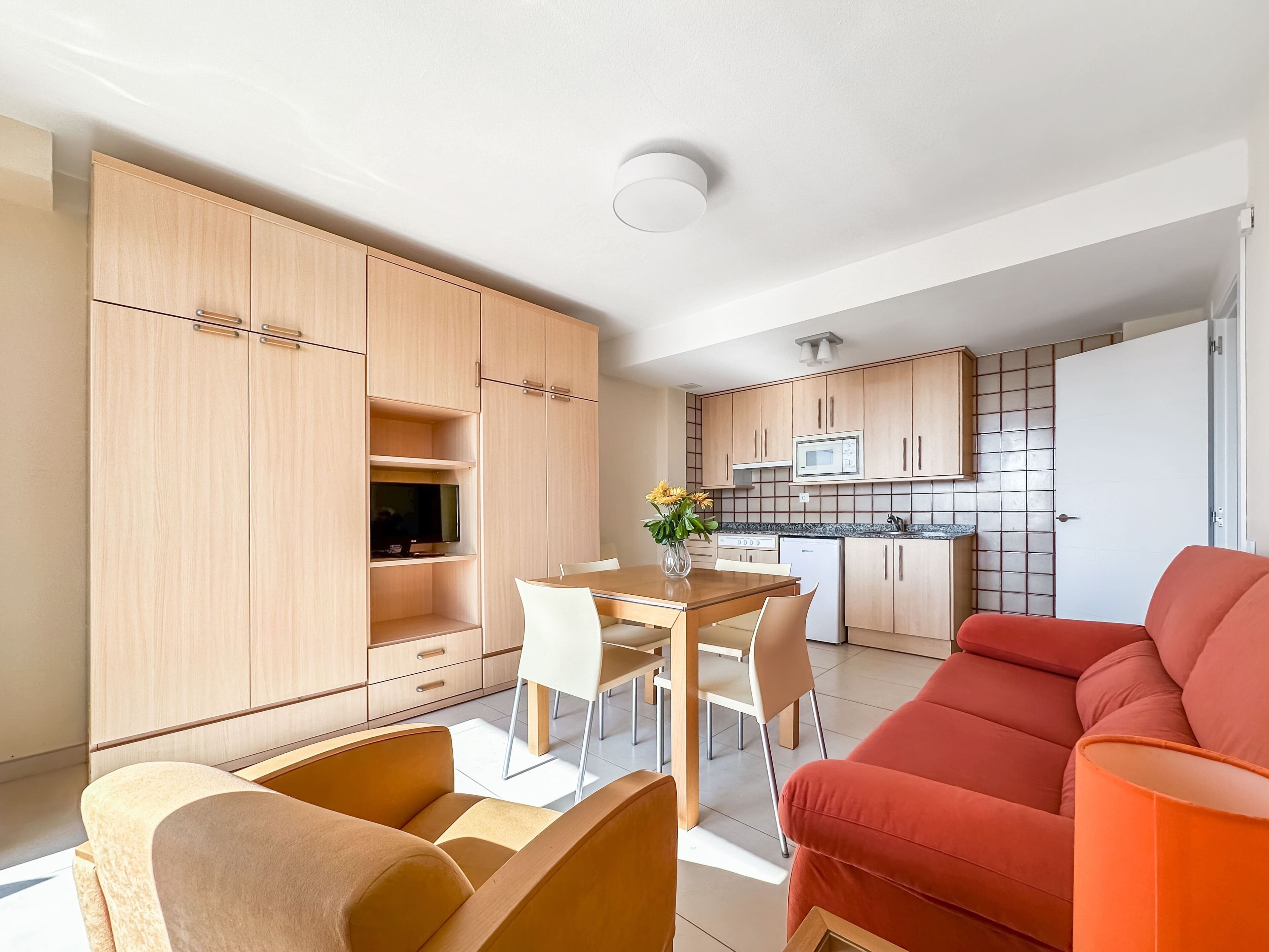 Una cucina moderna con armadietti in legno, un'area pranzo con tavolo e sedie, e un divano rosso.