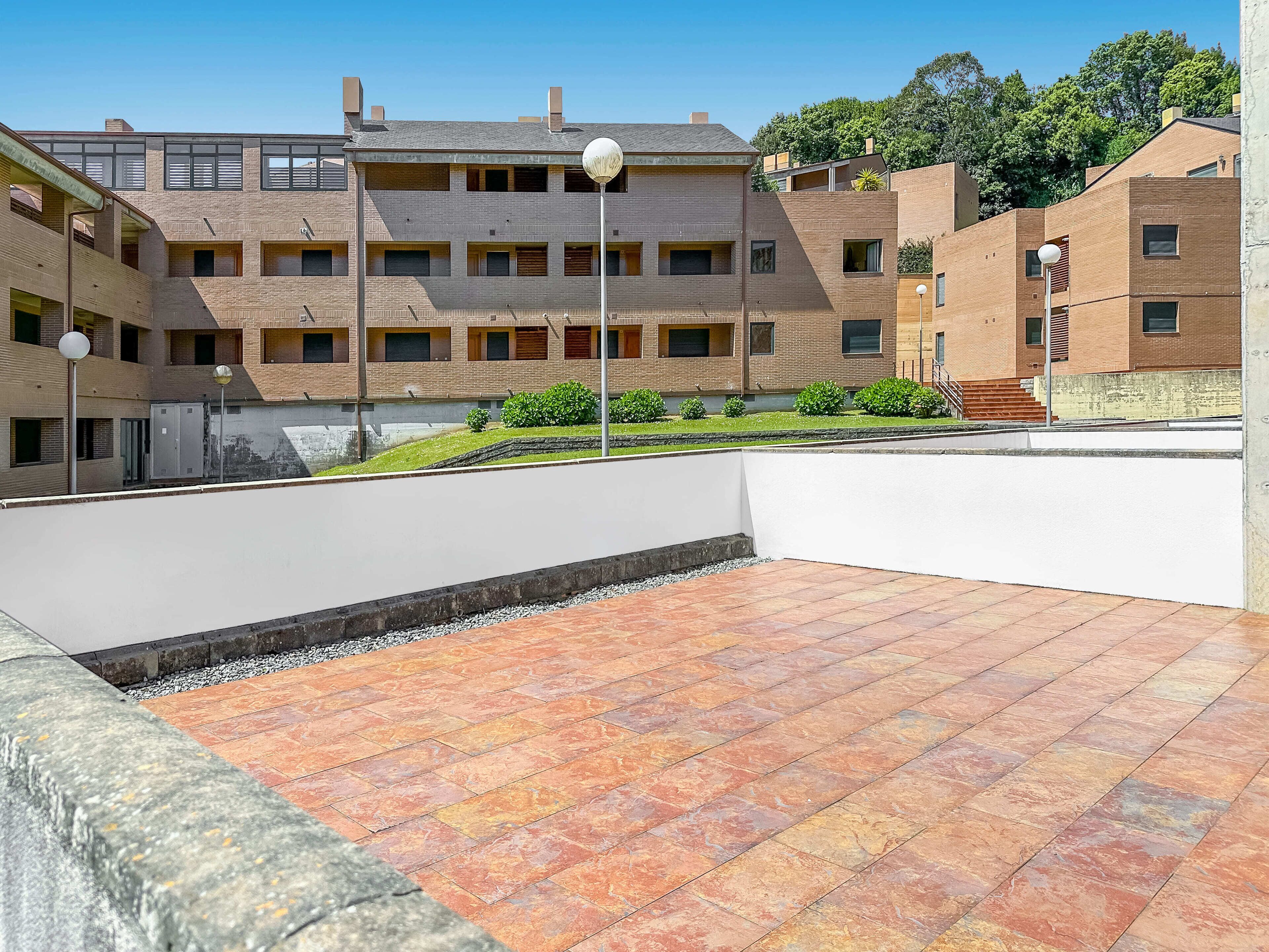 Una terrazza sul tetto con pavimento in piastrelle, un muro bianco e un edificio in mattoni sullo sfondo.