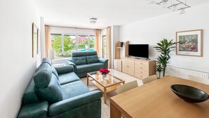 A modern living room with a sectional sofa, a TV, and a dining area with a table and chairs. - Apartamentos Solamaza (Arnuero)