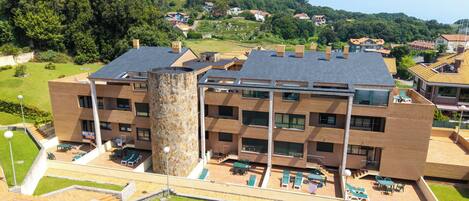 A multi-story building with a central tower, outdoor seating area, and a view of a hillside with houses.