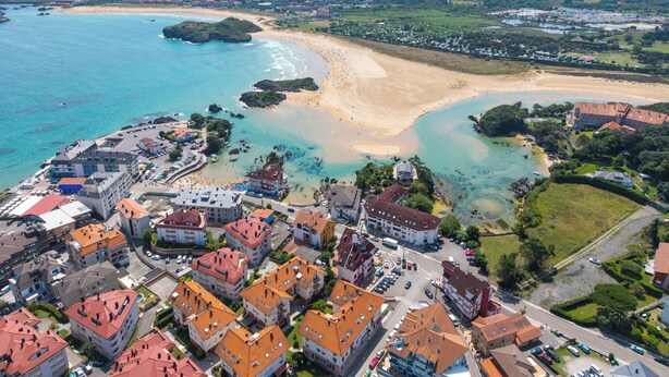 An aerial view of a coastal town with a beach, residential buildings, and a marina. - Apartamentos Solamaza (Arnuero)