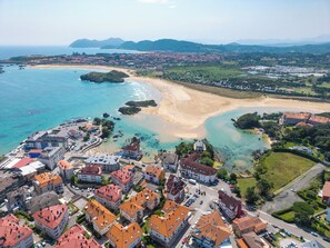 An aerial view of a coastal town with a beach, residential buildings, and a marina. - Apartamentos Solamaza (Arnuero)