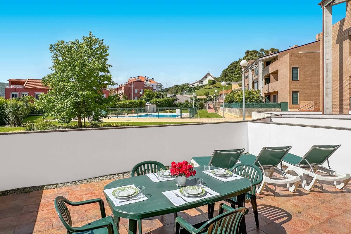 Terraza en la azotea con una mesa de comedor para cuatro, rodeada de sillas verdes, con vistas a una piscina y edificios residenciales.