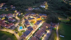 An aerial view of a residential area with multiple buildings, a swimming pool, and well-lit streets. - Apartamentos Solamaza (Arnuero)