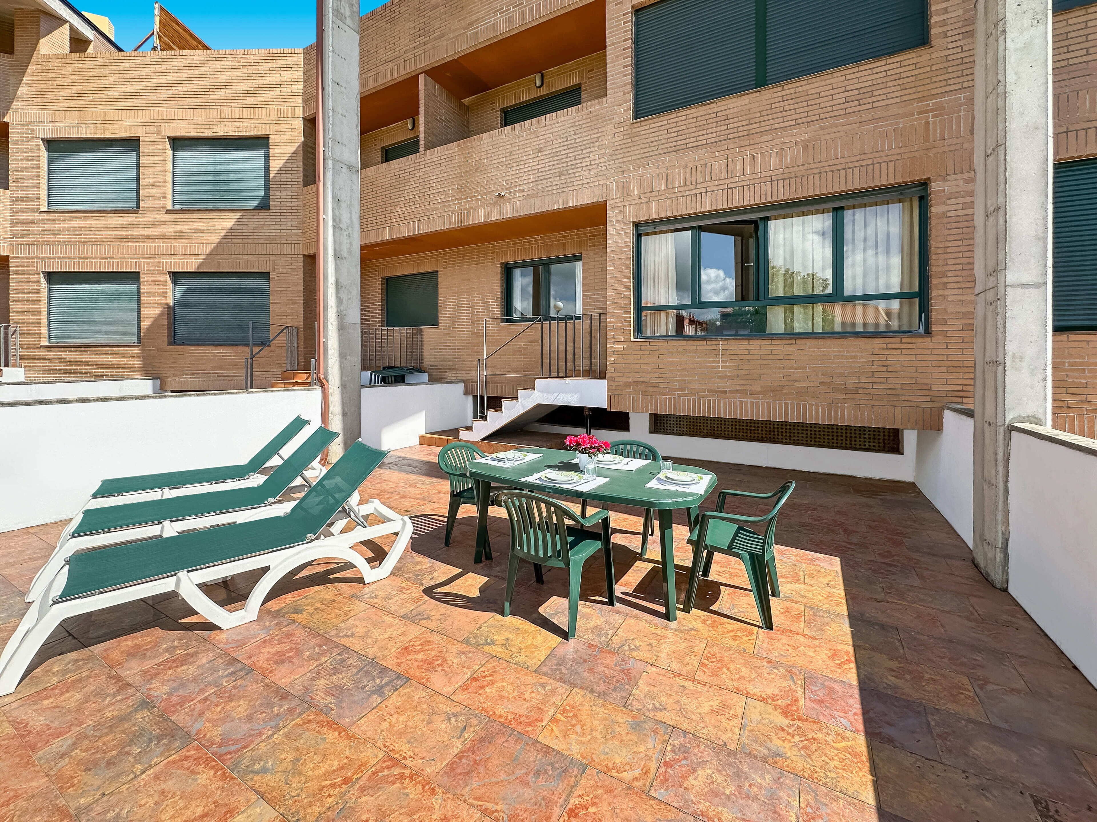 A rooftop terrace with lounge chairs, a table set for dining, and a staircase leading to an upper floor.