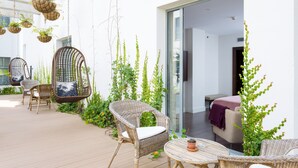 Un patio con mobiliario de mimbre, macetas colgantes y una puerta de vidrio que da a un espacio interior.