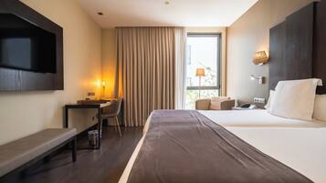 A hotel room with a bed, a desk, a chair, a TV, a window with curtains, and a lamp.
