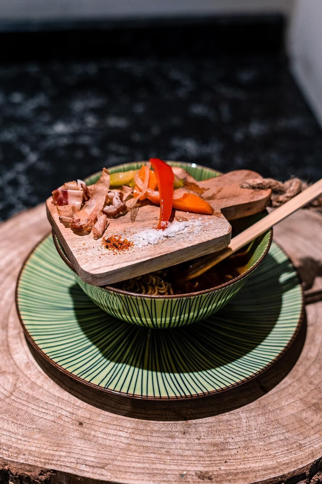 Un bol de nourriture avec une cuillère en bois, posé sur une assiette verte, lui-même placé sur une surface en bois.