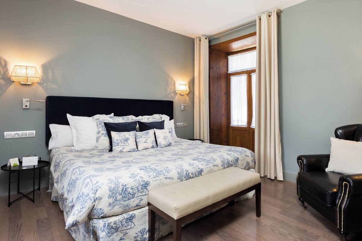 A hotel room with a large bed, a bench, a leather armchair, and a TV.