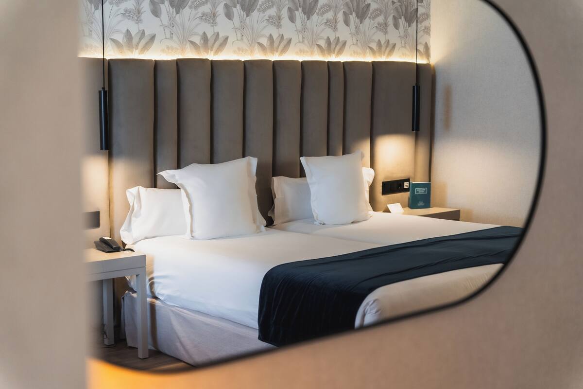A modern hotel room with a large bed, a bedside table with a phone, and a nightstand with a lamp.