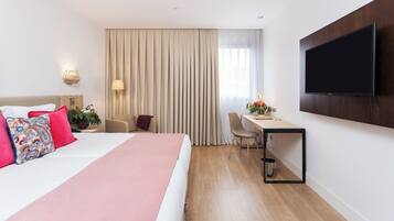 A hotel room with a bed, a desk, a chair, a TV, and a window with curtains.