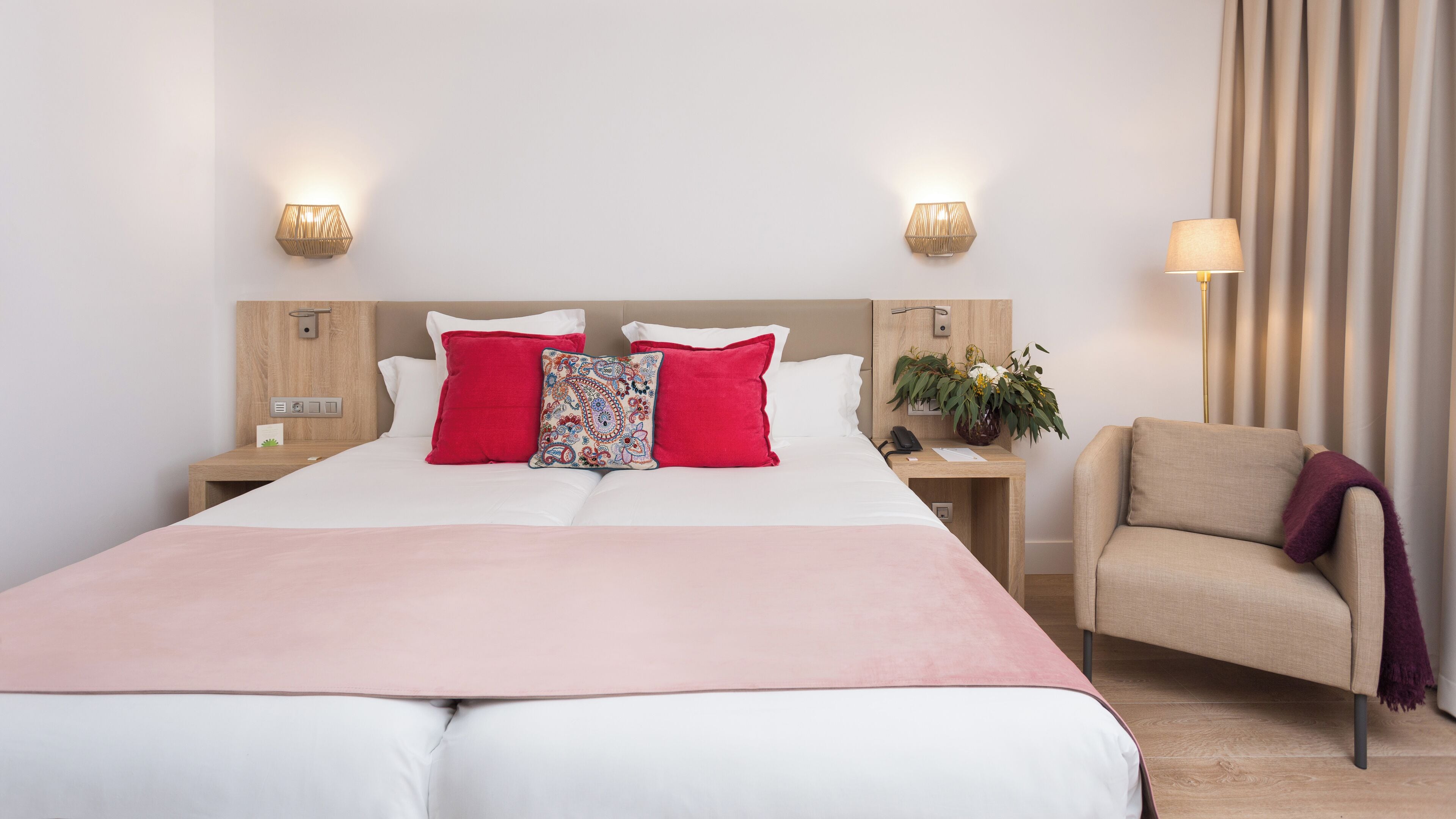 A hotel room with a bed, two bedside tables, a chair, and a wall-mounted lamp.